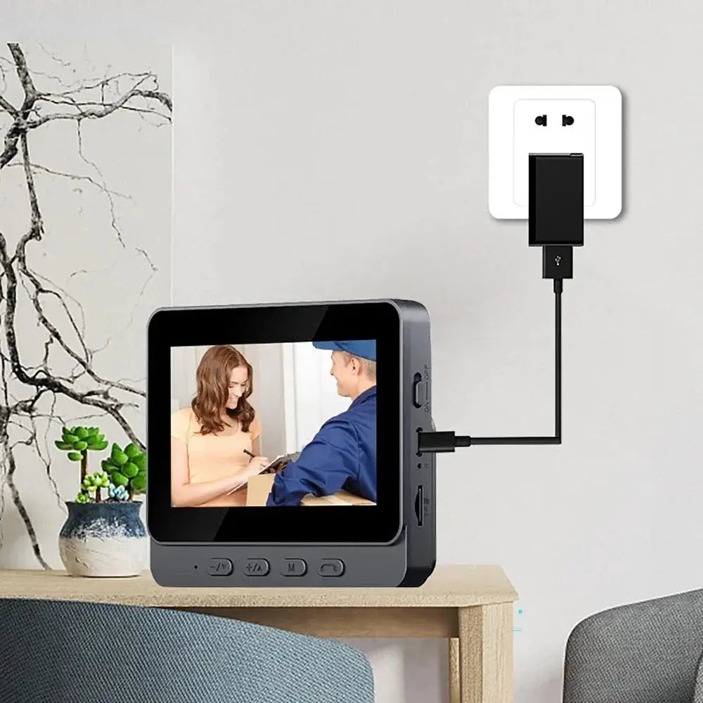 Black smart video doorbell with a 7 inch digital screen displaying a live feed of a woman and man interacting connected to a wall outlet via usb cable with night vision features.