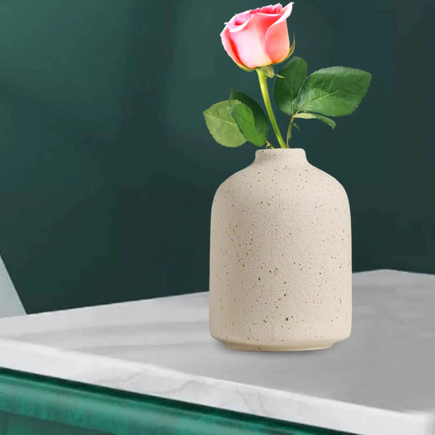 Cream-colored speckled ceramic flower vase holding a single pink rose for boho tabletop decor.