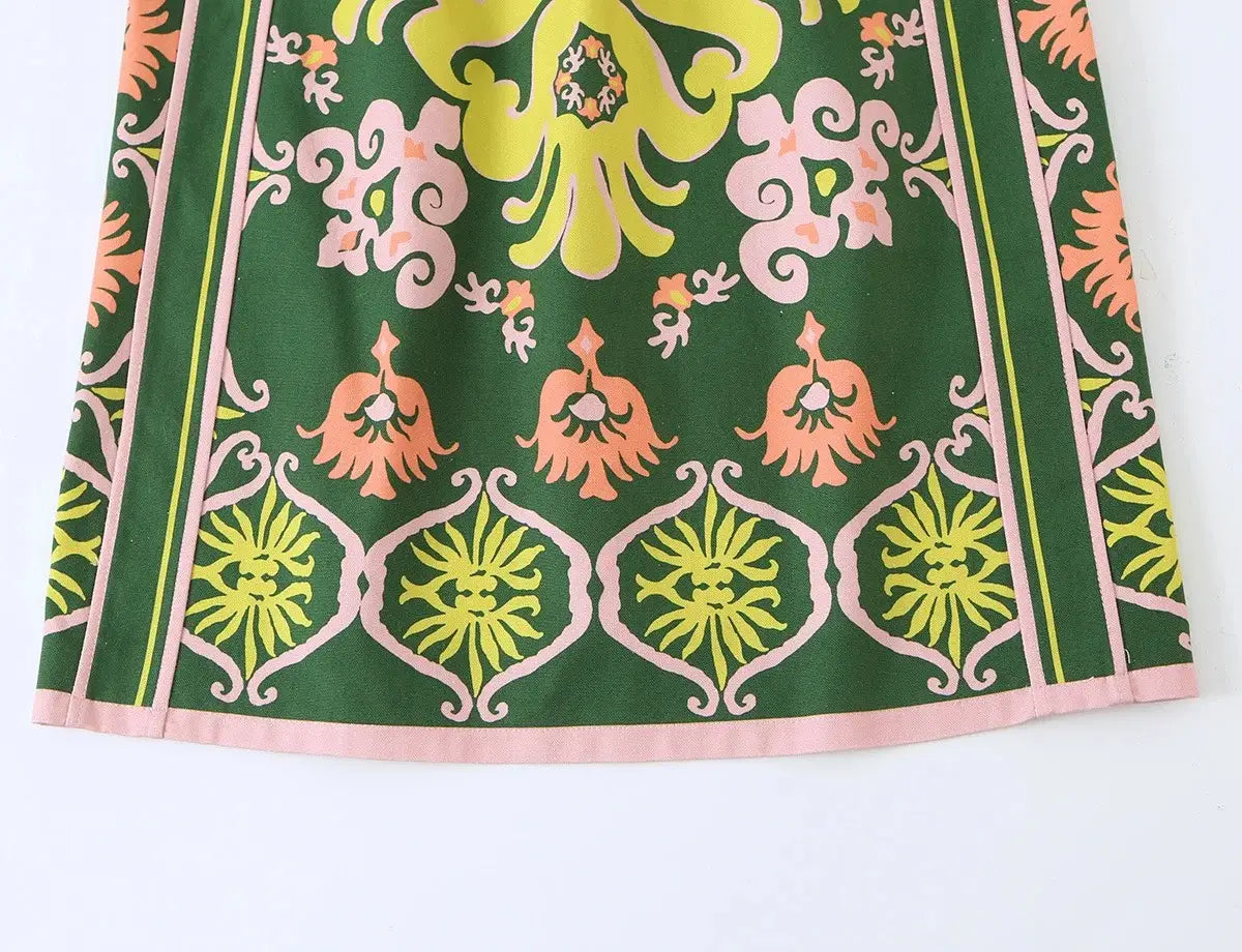 Ein leuchtend grünes florales zweiteiliges Midi-Rock-Set im Boho-Outfit-Stil mit einem kräftigen symmetrischen Muster aus gelben und pfirsichfarbenen Blumenmotiven und pinkfarbenen Akzenten am Saum.