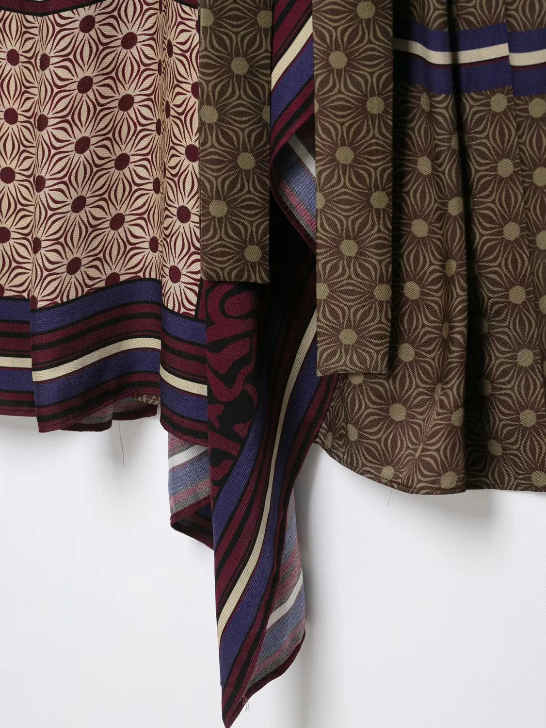 Ein fließender, gemusterter Schal mit geometrischem Design in erdigen Tönen aus Braun und Beige, akzentuiert durch kräftige Streifen in Navyblau, Maroon und Creme, vorgestellt mit dem Boho-Grafikdesign zweierlei Rockset.
