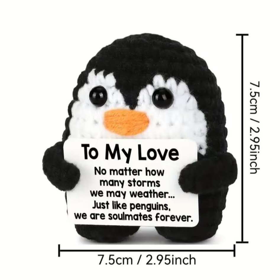 Un petit jouet en peluche au crochet de pingouin noir et blanc, avec un bec orange, tenant une pancarte sur laquelle il est écrit « À mon amour », en tant que cadeau d’amour au crochet de pingouin.