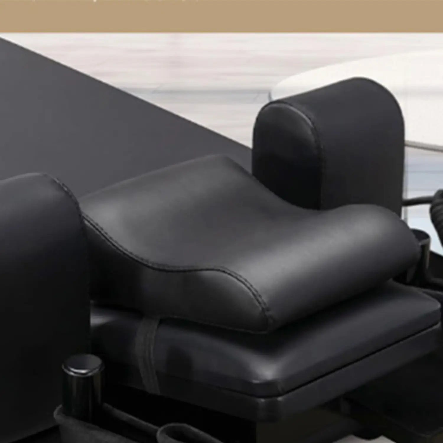 Black leather-backed ergonomic lumbar support pillow with contoured shape and stitched edges designed as a neck support pillow for Pilates reformer.