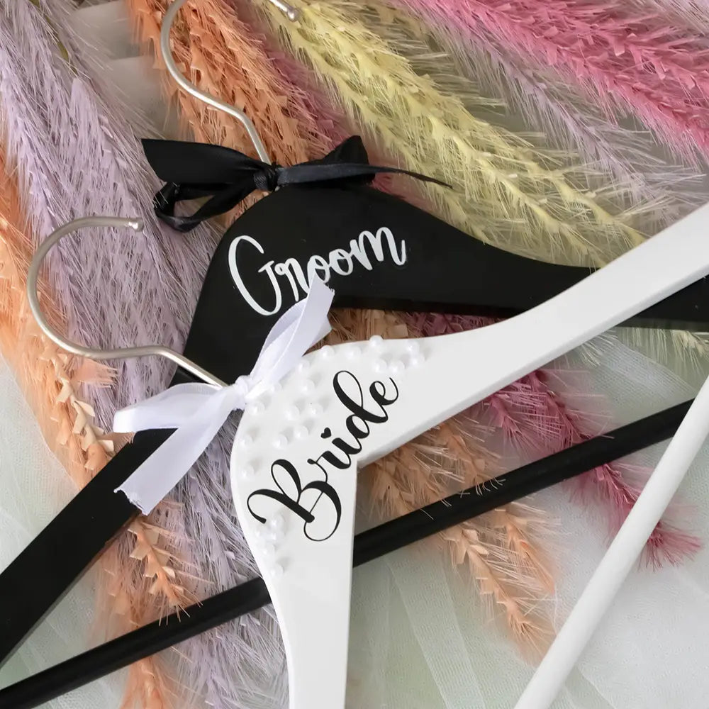 Cintre de mariage de la mariée en bois blanc, avec lettres cursives noires et un nœud en ruban blanc, provenant de l’ensemble de cintres de mariage perles pour la mariée et le marié.