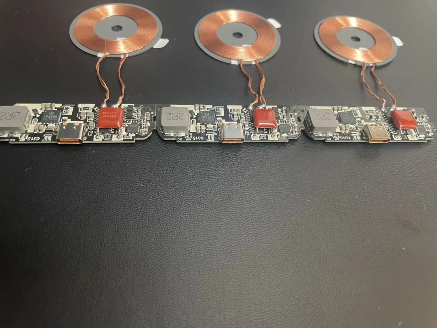 Trois bobines de charge sans fil recouvertes de cuivre montées sur des cartes de circuit imprimé identiques avec des ports USB-C et des condensateurs rouges pour une carte PCBA de module de charge sans fil 15 W à charge rapide