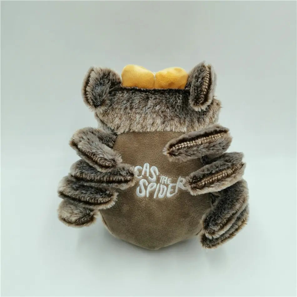 A plush toy cartoon spider stuffed animal doll made in mainland China featuring gray fuzzy fur, a yellow bow on its head, and embroidered cas the spider text on the back.
