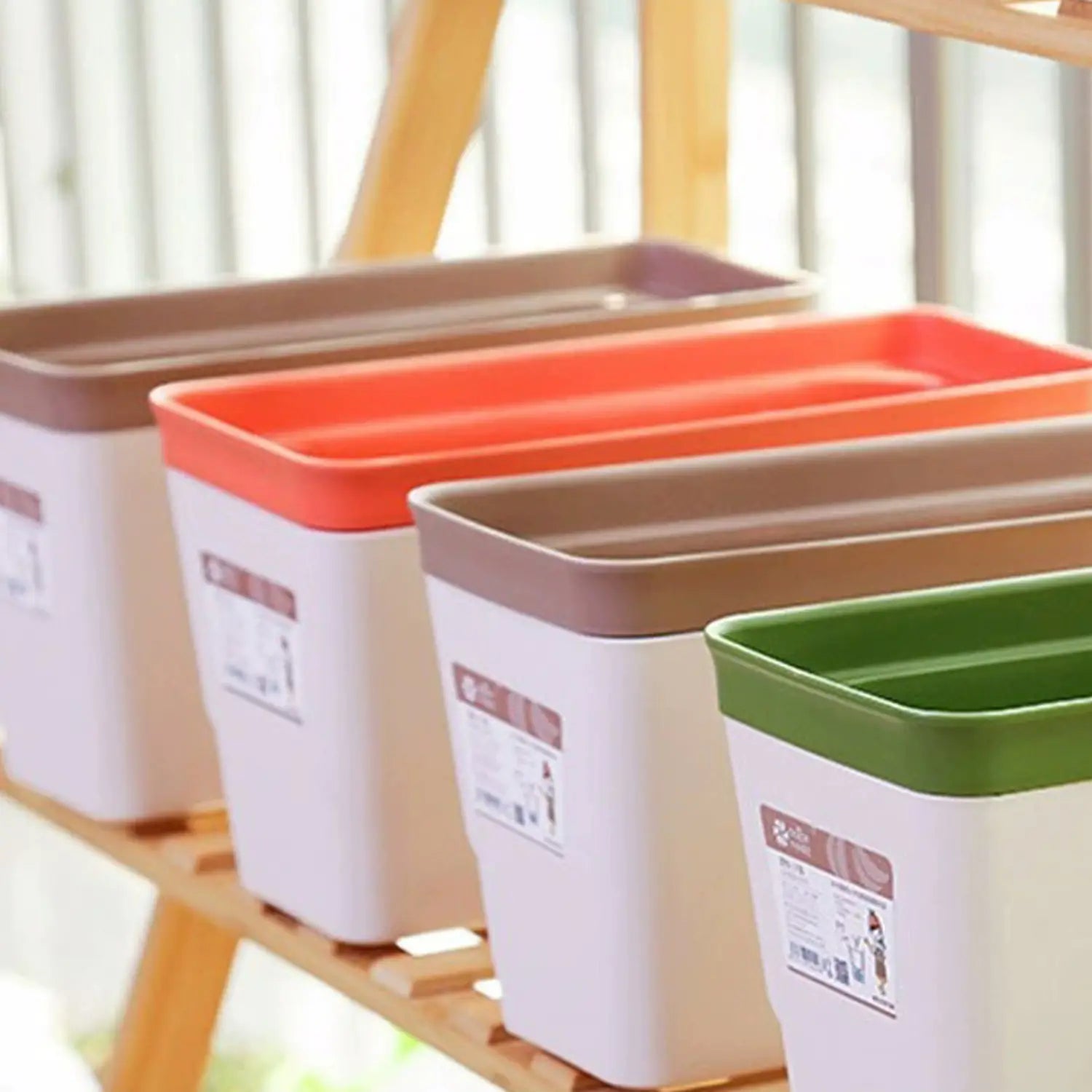 Set aus vier selbstbewässernden rechteckigen Kunststoff-Blumentöpfen mit automatischer Bewässerungsfunktion, Baumwollstreifen und farbigen Deckeln in Braun, Orange, Grün und Beige.