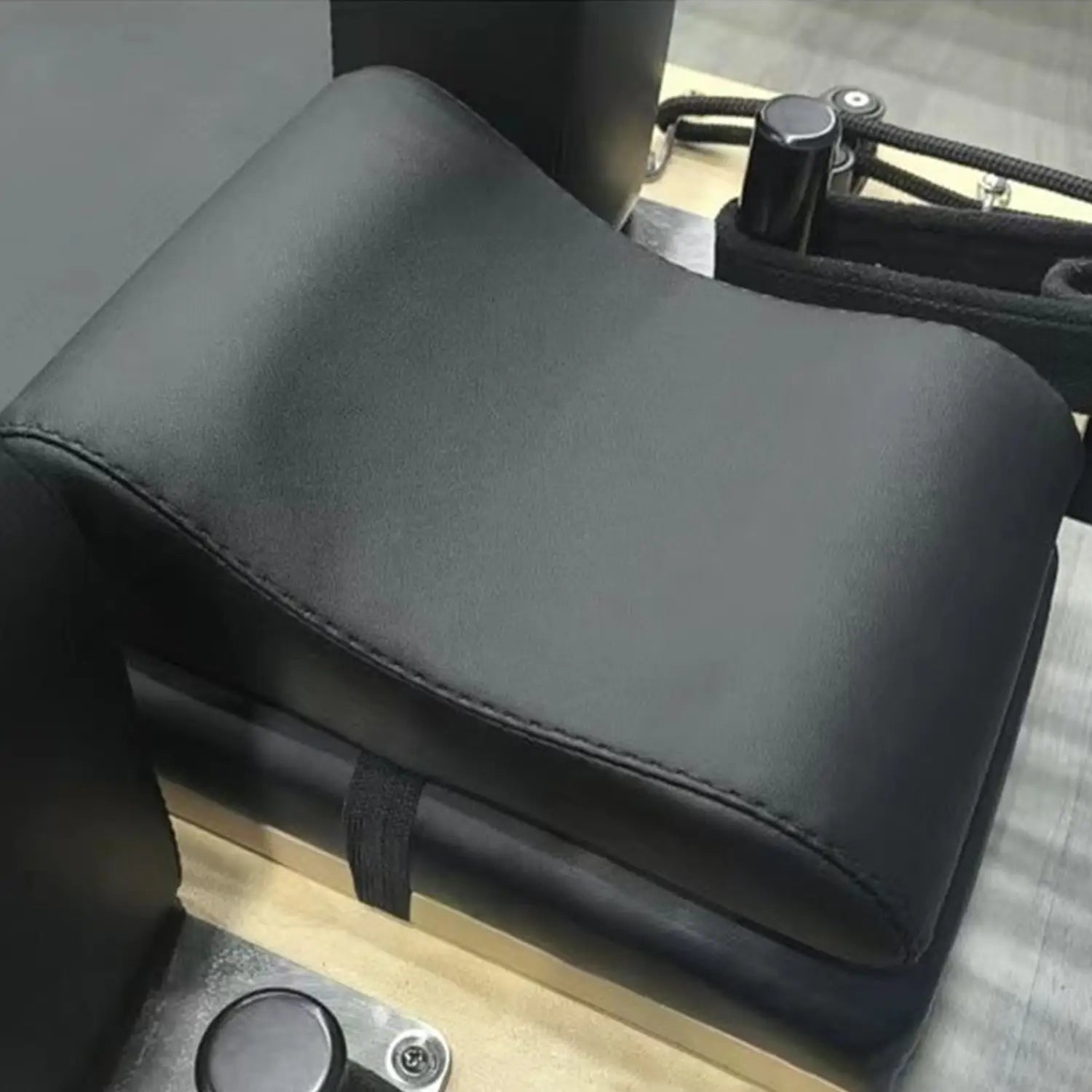 Black leather neck support pillow with stitched edges and padded contoured design for Pilates reformer.