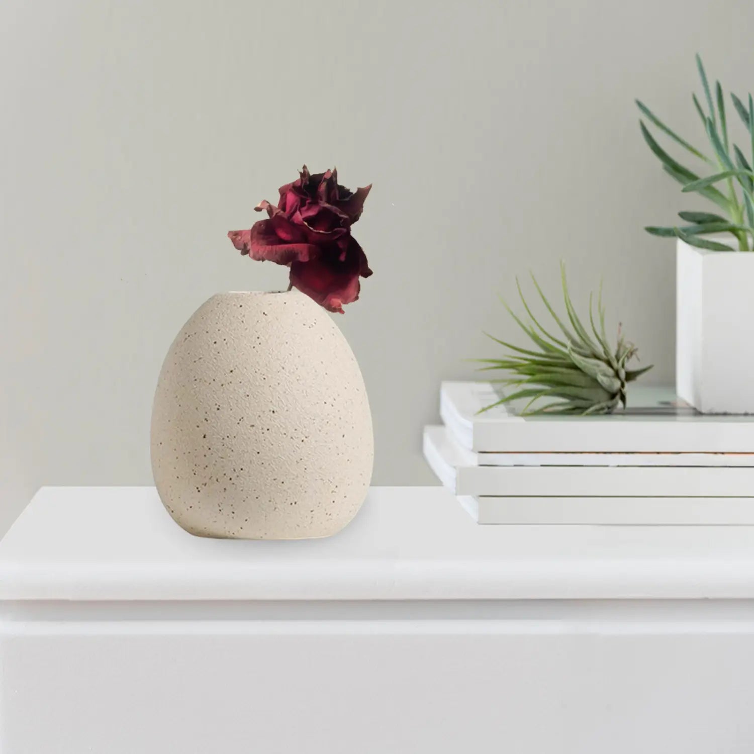Cream-colored speckled ceramic flower vase holding a dried burgundy rose for boho tabletop decor.