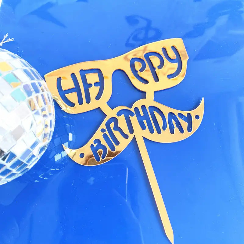 Gold-colored acrylic Father’s Day cake topper shaped like sunglasses and a mustache with happy birthday engraved in blue for super dad celebration.