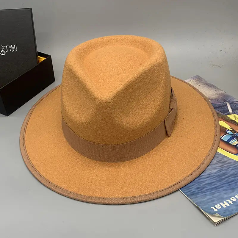 A tan woolen felt fedora hat with a matching brown ribbon band and stitched detailing featuring a feather accent for unisex wear.