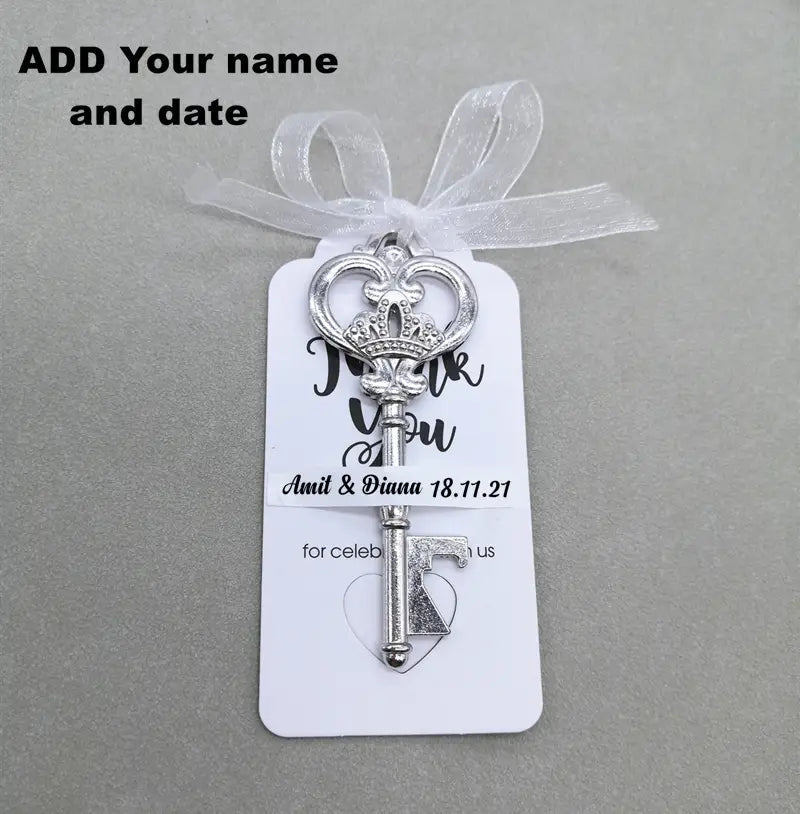 Encanto de llave ornamentada en plata con diseño de corona, sujeto a una etiqueta blanca y cinta para recuerdos abridores de botellas para bodas personalizados.