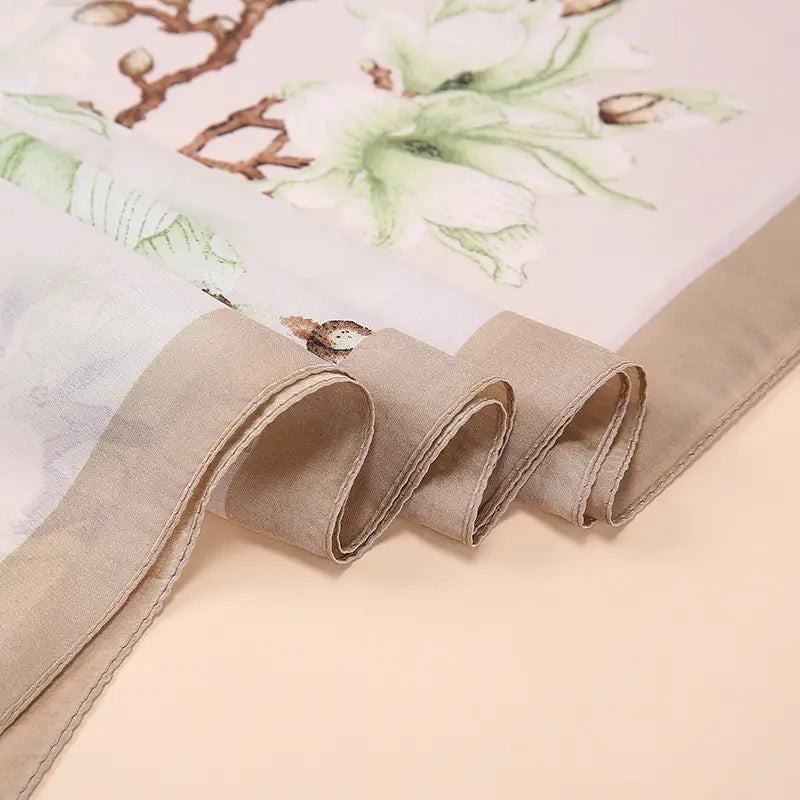 Un foulard en soie beige délicat, présentant un imprimé aquarelle doux de magnolias verts et de branches brunes, issu de la collection des amandiers en fleurs de Van Gogh.