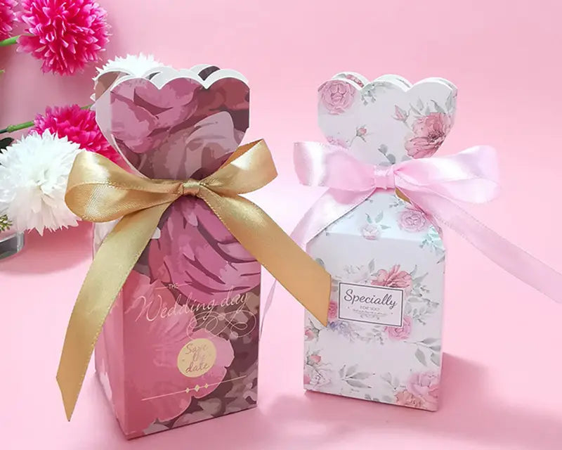 Zwei Hochzeits-Gastgeschenkboxen mit Schleifen, in sanftem Rosa mit einem goldfarbenen Band sowie in Weiß mit einem hellrosa Band, für eine elegante Geschenkverpackung.