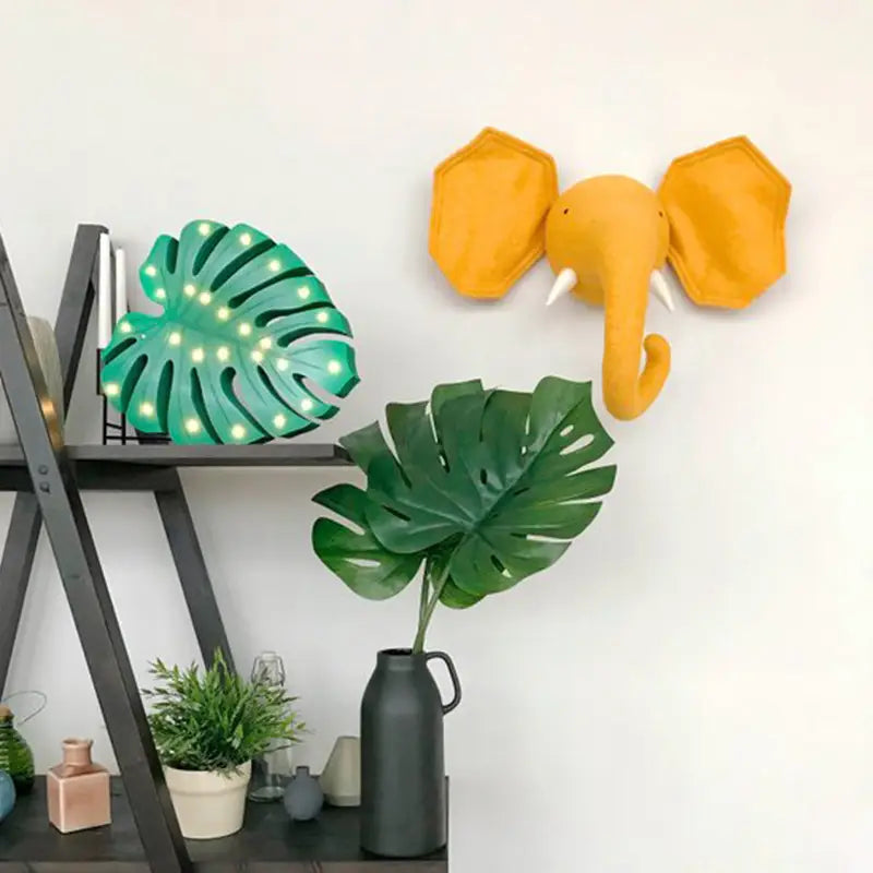 Eine gelbe geometrische Elefanten-3D-Cartoon-Tierkopf-Wanddekoration mit weißen Stoßzähnen aus leichtem Material für die moderne Inneneinrichtung.