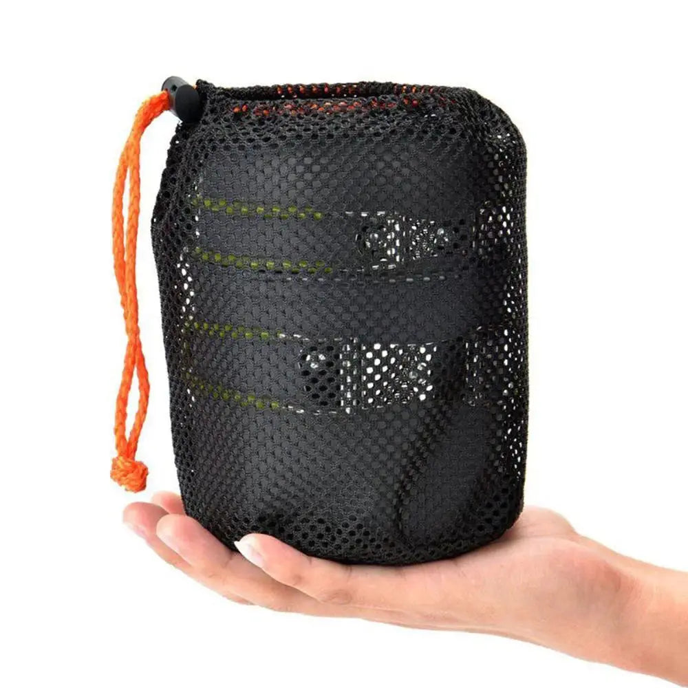 Schwarze Mesh-Tragetasche mit orangefarbenem Kordelzug und schwarzem Kunststoff-Toggle, ausgelegt zur Aufnahme eines kompakten Camping-Kochgeschirr-Sets mit Herd und Töpfen.