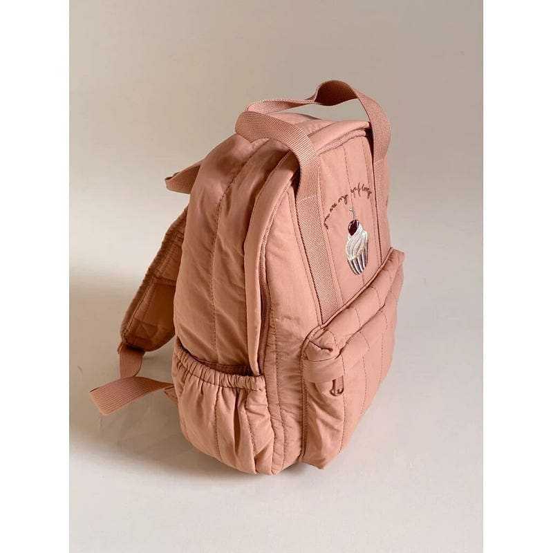Ein weicher blush pinkfarbener gesteppten Kinder-Rucksack aus wasserfestem Material mit einem niedlichen Cupcake-Patch auf der Vorderseite, geeignet für den Schulgebrauch.