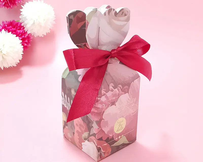 Eine Blumige Hochzeits-Gastgeschenkbox mit rosafarbenem, blumig gemustertem Papier und einem leuchtend roten Satinband, in Form einer Schleife gebunden