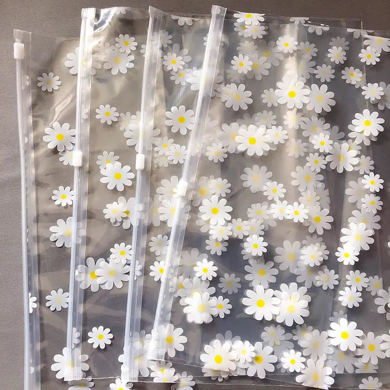 Klare Kunststoff-Reißverschlussbeutel aus transparentem Material mit einem sich wiederholenden Muster aus weißen Gänseblümchen mit gelben Zentren, gestaltet als blumige, durchsichtige Reisekosmetiktaschen.