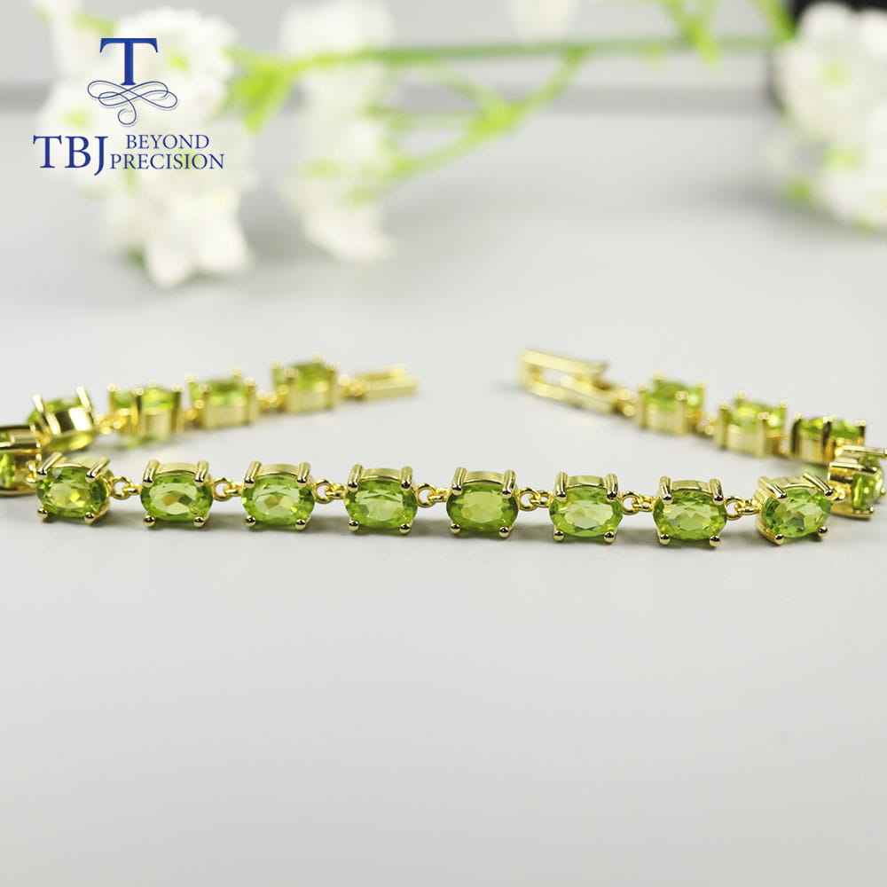 Una pulsera tipo tenis delicada de plata de ley con peridoto, con engastes en tono dorado, que presenta una fila de piedras ovaladas color verde.