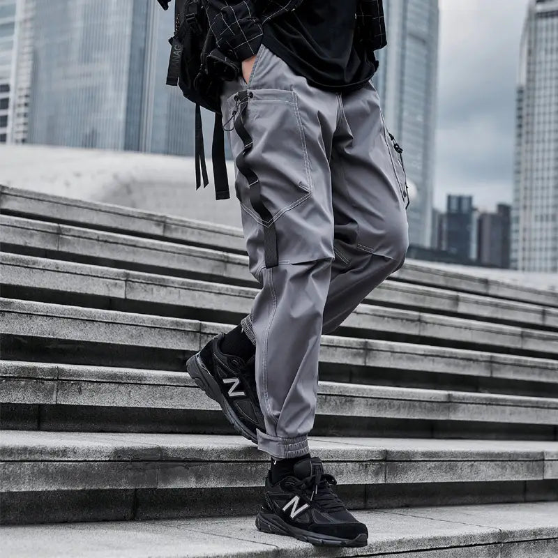 Herren schwarze taktische Cargo-Jogginghosen mit grauer Cargo-Hose, mehreren Taschen und schwarzen Stoffriemen an den Seiten, entworfen für Streetwear-Einsatz.