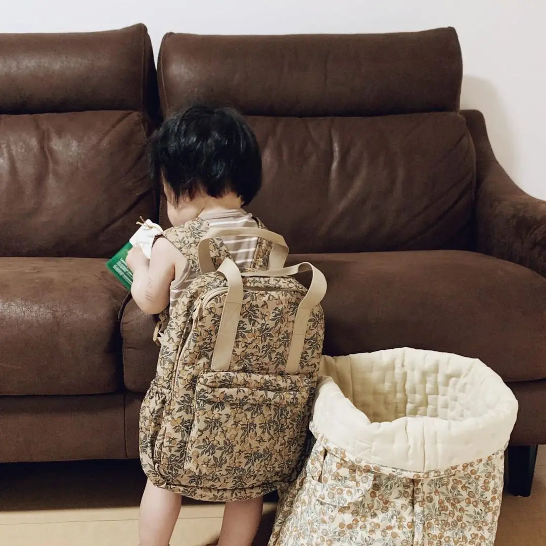 Ein Kind mit einem beigen Kinder-gesteppten Rucksack mit floralem Muster und besticktem Design, mit hellbraunen Trägern, der als wasserfester Schulrucksack von der Rückseite gezeigt wird