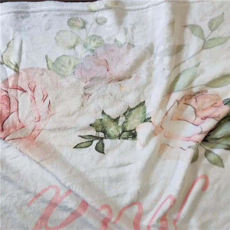 Personalisierte Baby-Wickeldecke aus Fleece in sanftem Off-White mit einem zarten Blumenmuster im Stil einer Aquarellzeichnung, mit rosafarbenen Rosen und grünen Blättern.