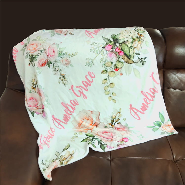 Personalisierte Baby-Wickeldecke aus Fleece in sanftem hell-minzgrün mit zarten rosa- und pfirsichfarbenen Rosen sowie grünem Blattwerk, bestickt mit dem Namen Amelia Grace in fließender Schreibschrift.
