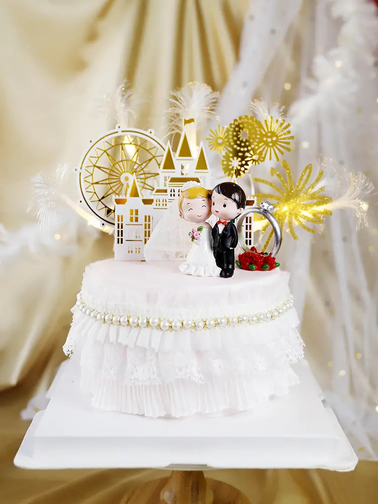 white wedding cake topper featuring a bride and groom acrylic figurine with gold castle and ferris wheel decorations accented by red roses and a silver ring.