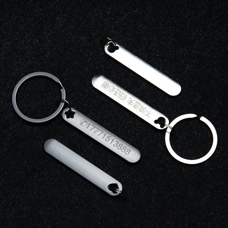 Silver metallic custom phone number keychains with laser engraved text and heart-shaped cutouts on a metal key ring.