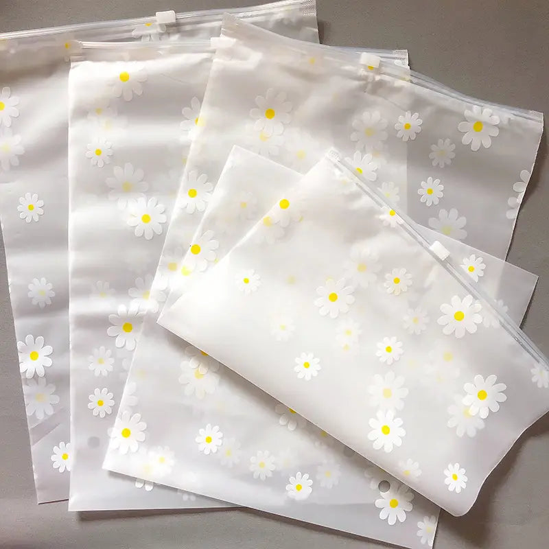 Blumige, durchsichtige Reisekosmetiktasche aus durchsichtigem Kunststoff mit Reißverschlussbeuteln und einem zarten Muster aus weißen Gänseblümchen mit gelben Zentren.