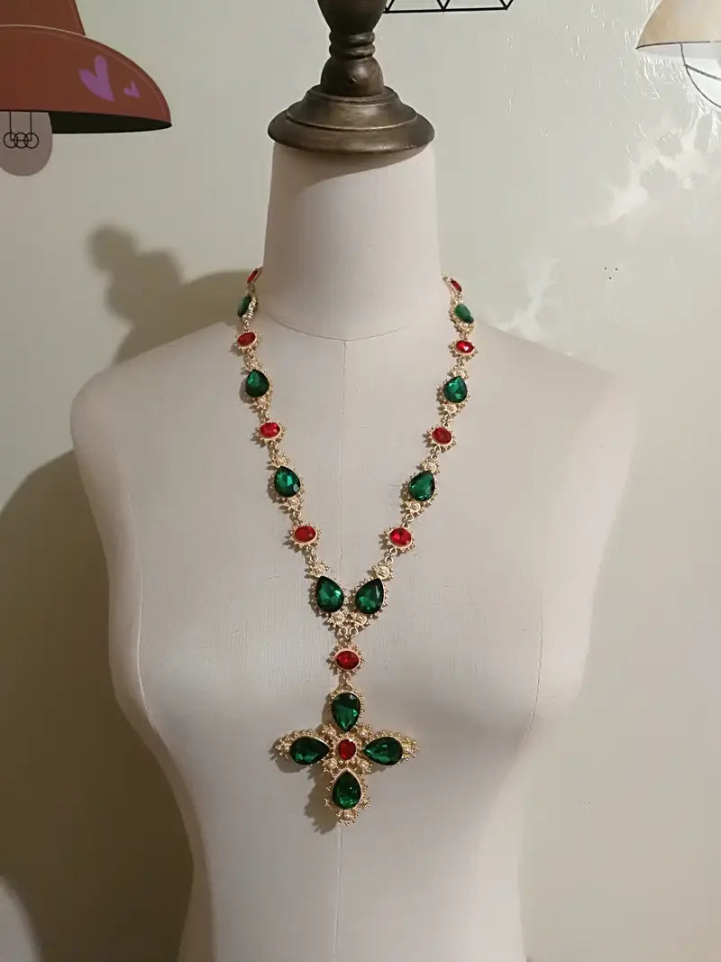 Collier ras du cou à déclaration en cristal à finition dorée, étincelant, avec des pierres alternées vert émeraude et rouge rubis en forme de larme, disposées dans une conception de pendentif en forme de croix, pour des bijoux de soirée.