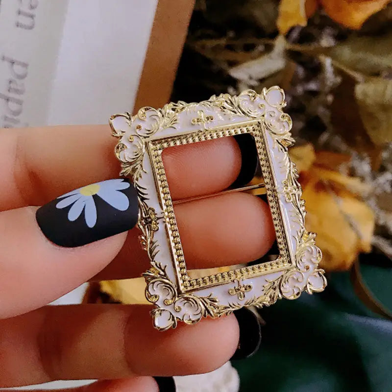 Broche delicado para marco de cuadro con arte de David barroco, con acabado esmaltado dorado y marfil, con detalles florales intrincados a lo largo de su ornamentado borde.