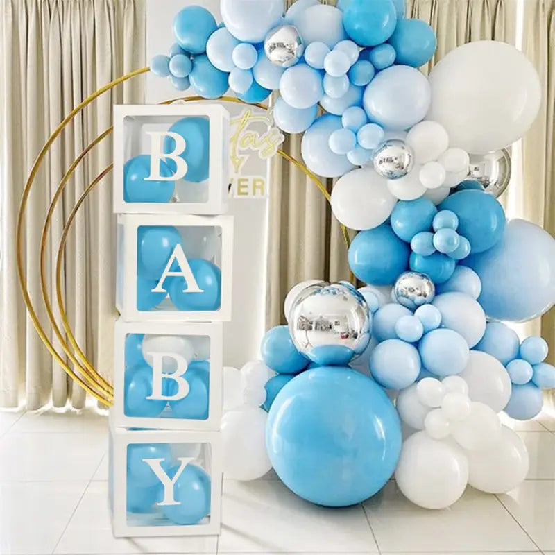 Un arco decorativo de globos en color azul claro, blanco y plateado presenta un elegante grupo de globos como parte de un juego de caja con globos transparente para baby shower.