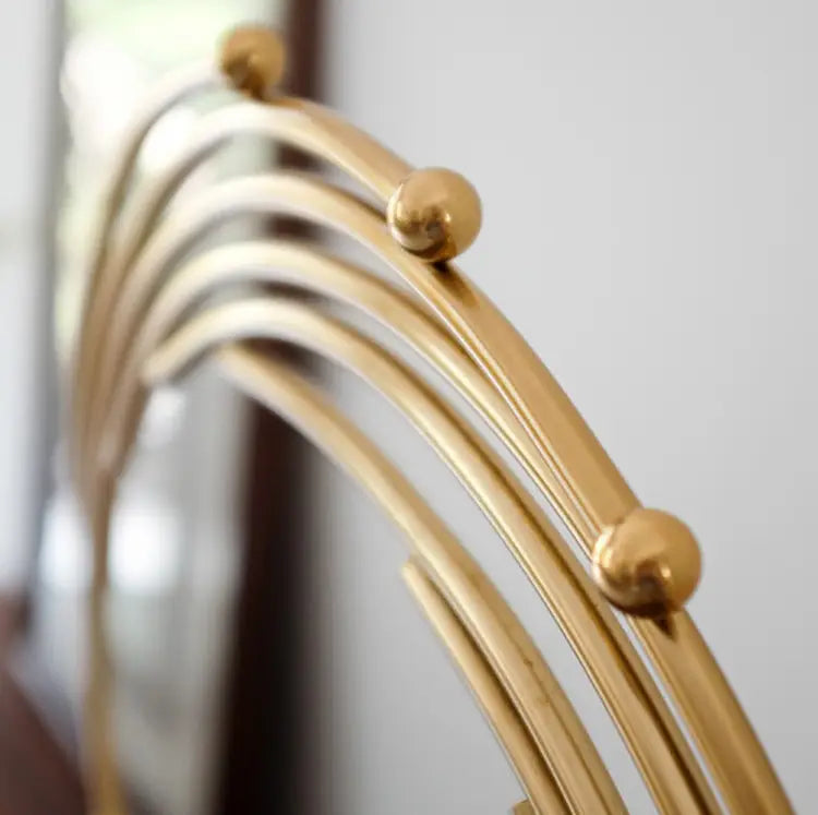 Gold metal abstract sculpture office desk decor with a gold-toned metal mirror frame featuring a curved arched design and spherical accents.