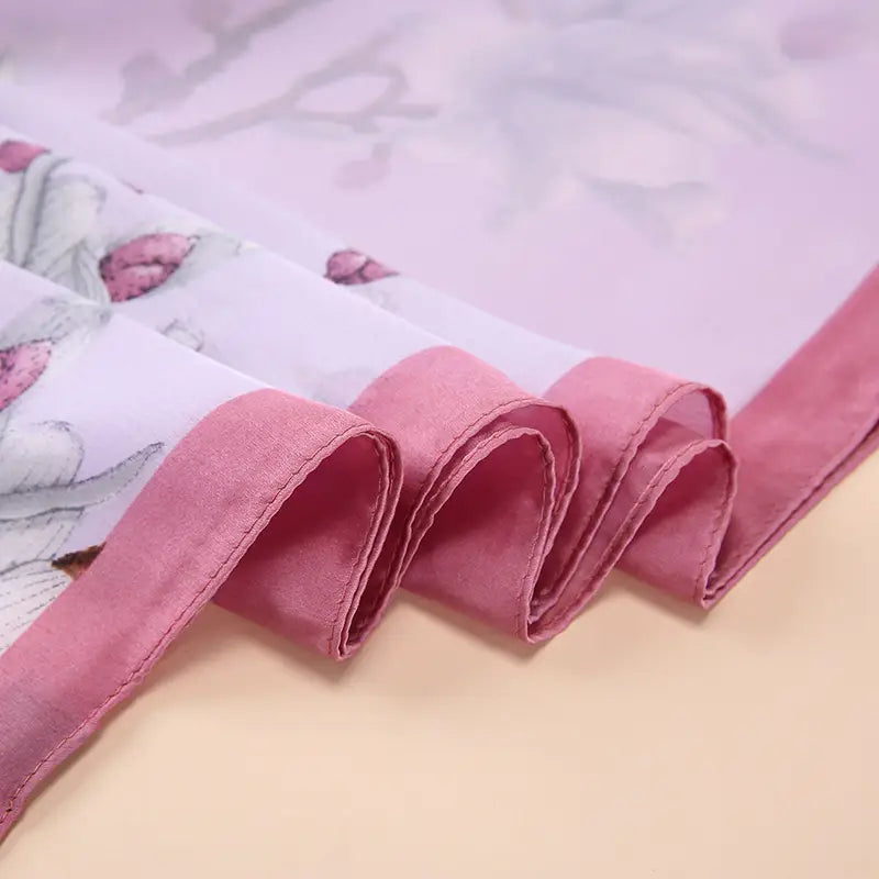 Le châle foulard en soie « Van Gogh Almond Blossom » présente un tissu transparent délicat à motifs floraux roses, une finition douce façon satin et des bords soigneusement cousus.
