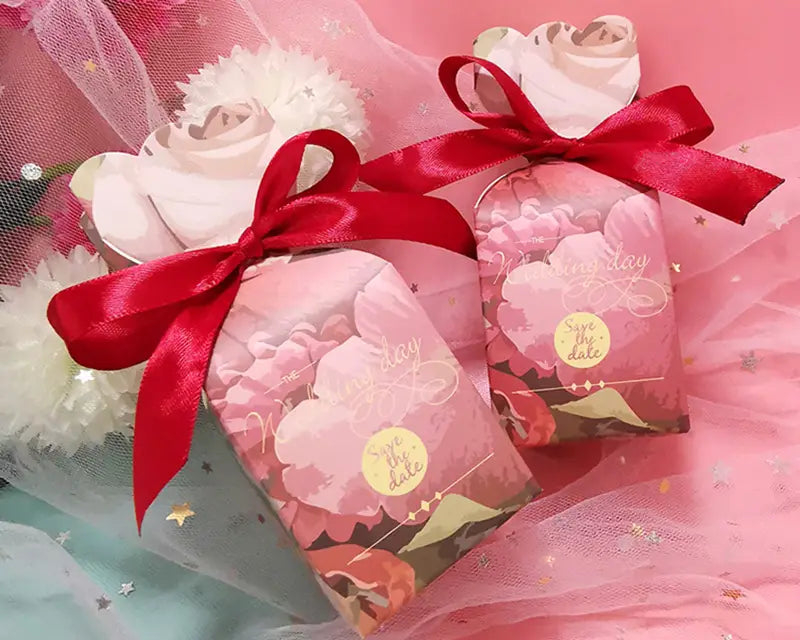 Rosa blumige Gastgeschenkboxen aus Papier, gebunden mit roten Satinbändern, für elegante Geschenke bei besonderen Anlässen.