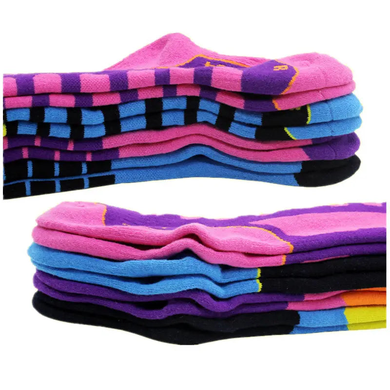 Pile de chaussettes de ski rayées colorées en rose, violet, bleu et noir, avec des accents jaune néon, fabriquées en coton épais pour les sports d’hiver en famille thermiques.
