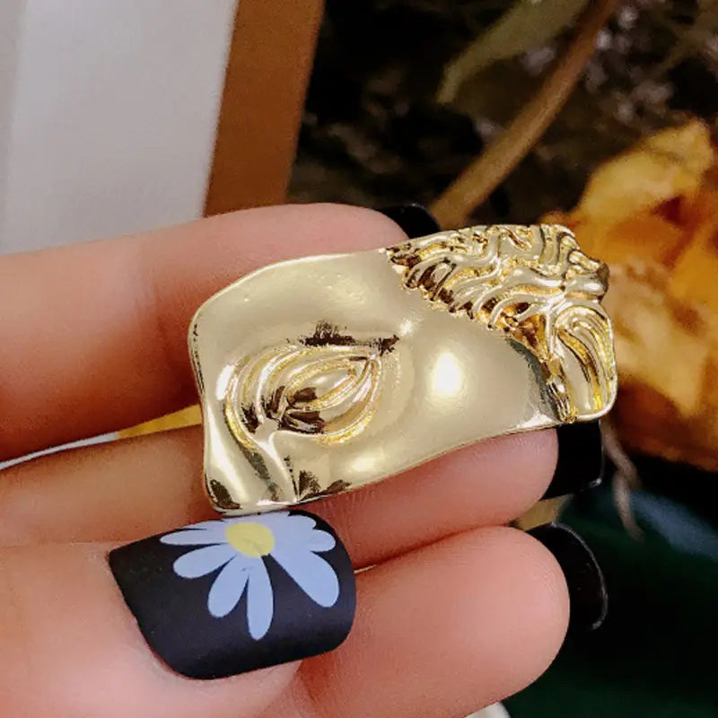 Anillo escultórico en tono dorado con diseño de cara en forma de medio arco, con detalles intrincados y acabado brillante, en el estilo de broche para marco de cuadro con arte de David barroco.