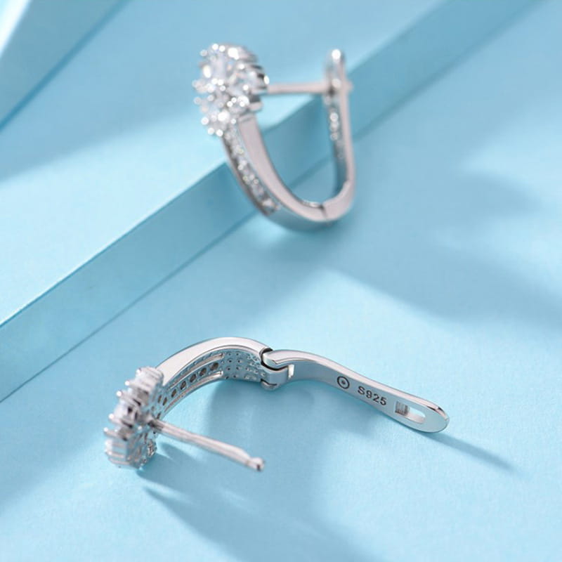 Sterling silver zircon flower hoop earrings feature silver huggie hoops adorned with a cluster of sparkling clear stones set in a polished metal frame.