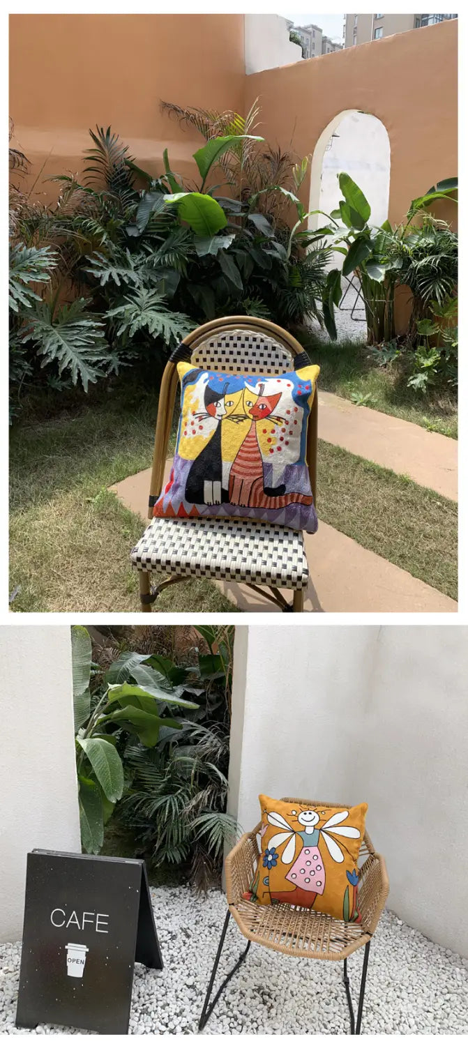 Une housse de coussin colorée et éclatante 45 x 45 cm avec un design de bande dessinée abstraite brodé, présentant deux personnages stylisés reposant sur une chaise en osier