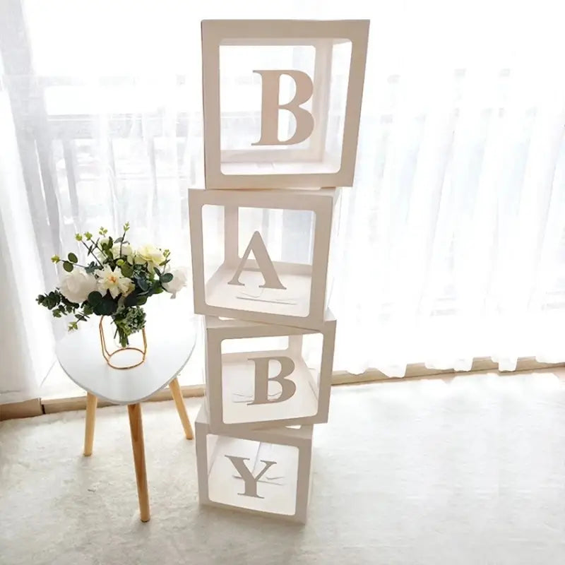 Letras de bloques para bebé blancas apiladas con letras mayúsculas de tono plateado, en un juego de caja con globos transparente para baby shower.