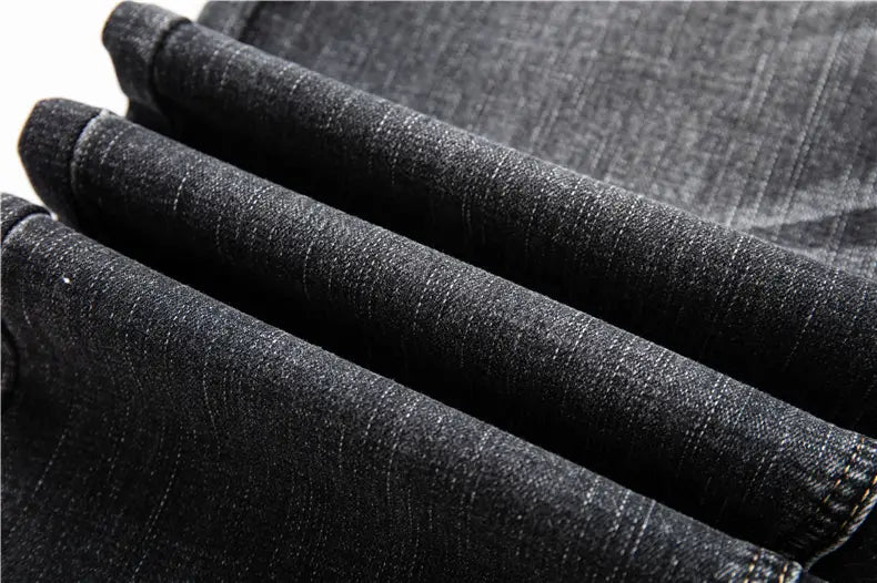 Jeans en denim stretch pour hommes, coupe regular fit, en tissu denim foncé, présentant une trame texturée subtile et des coutures visibles le long des revers retroussés.