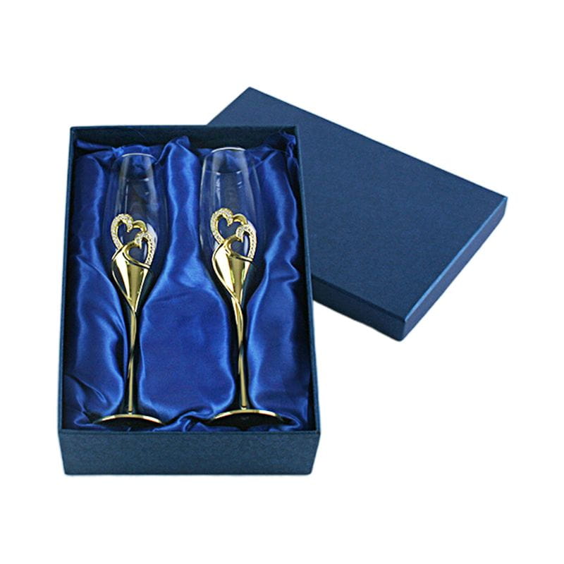 A pair of elegant gold-finished wedding champagne flutes with intertwined heart designs nestled in a luxurious blue satin-lined gift box.