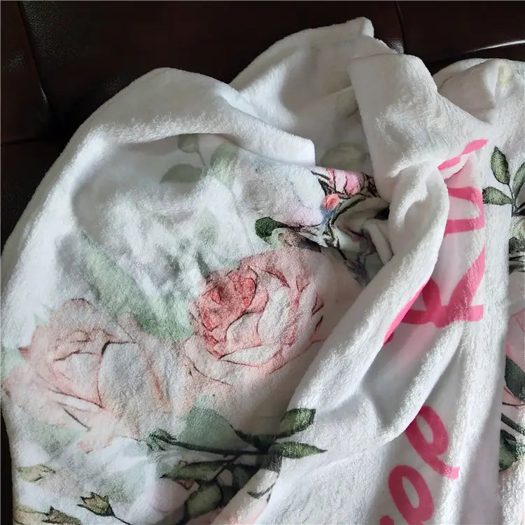Personalisierte Baby-Wickeldecken-Fleece in Weiß mit sanften rosa- und grünen floralen Mustern und kräftiger pinkfarbener Beschriftung.