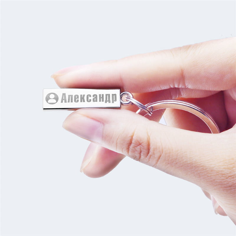 Silver rectangular personalized engraved metal anti-lost keychain with a cyrillic name alexandr and a small profile icon attached to a matching metal ring.