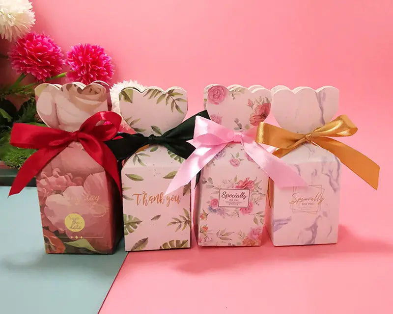 Drei Hochzeits-Gastgeschenkboxen mit Blumenmuster aus Papier mit gewellten Oberkanten, jeweils mit einem Satinband in Rot, Schwarz oder Gold gebunden.