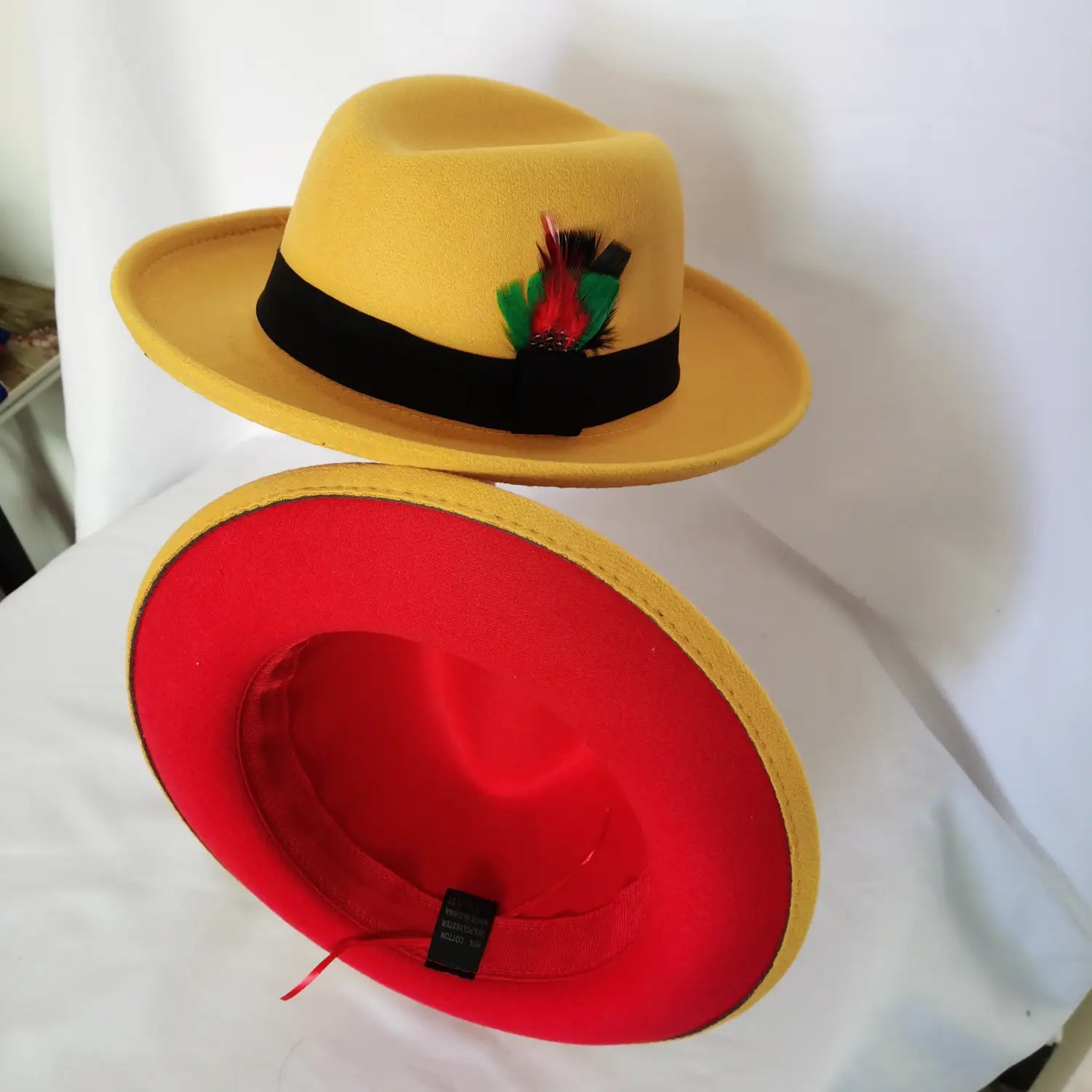 Unisex woolen felt fedora hat in yellow featuring a black band with colorful feather accent and red interior lining.