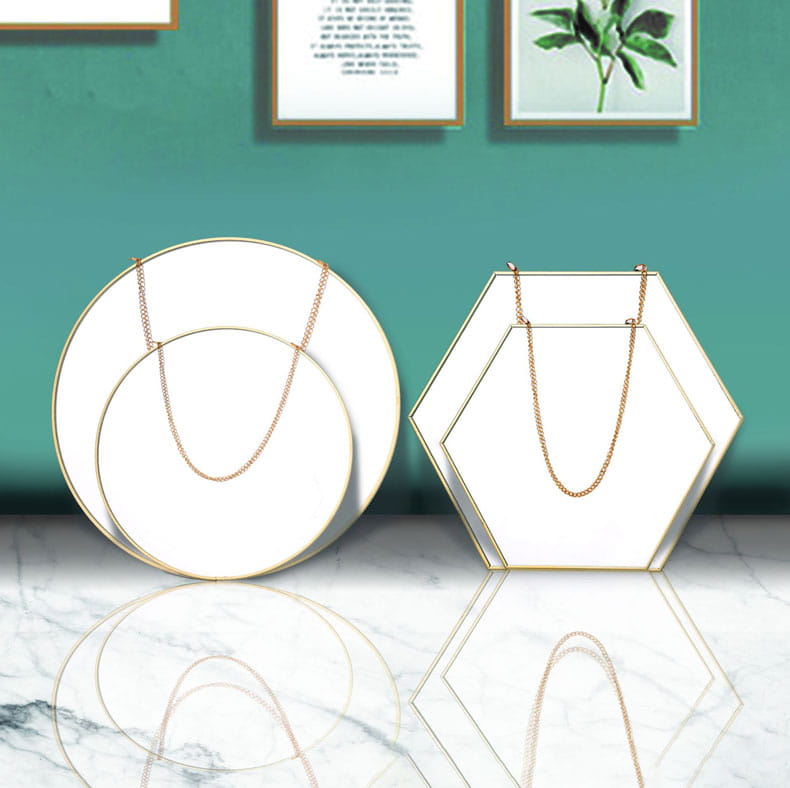 gold chain necklace displayed on white geometric stands alongside a gold hexagonal wall hanging mirror
