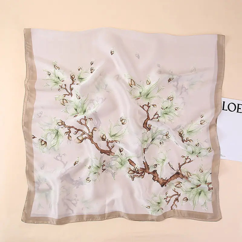 Un foulard en soie ivoire délicat, présentant un motif botanique élégant de branches brunes, des feuilles vert clair et des bourgeons, encadrés par une bordure beige subtile, issu de la collection de châles foulards en soie « Van Gogh Almond Blossom ».