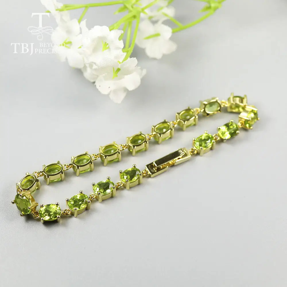 Una pulsera tipo tenis delicada de plata de ley con peridoto, con eslabones en tono dorado y piedras ovaladas de peridoto dispuestas de manera uniforme, en un diseño clásico.